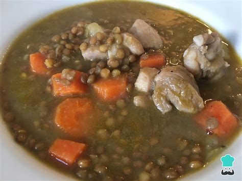 Plato humeante de guiso de lentejas con trozos de pollo y verduras variadas.