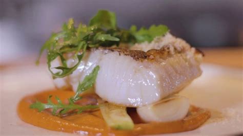 un filete grueso de merluza austral frita servido sobre una cama de puerros y tomates