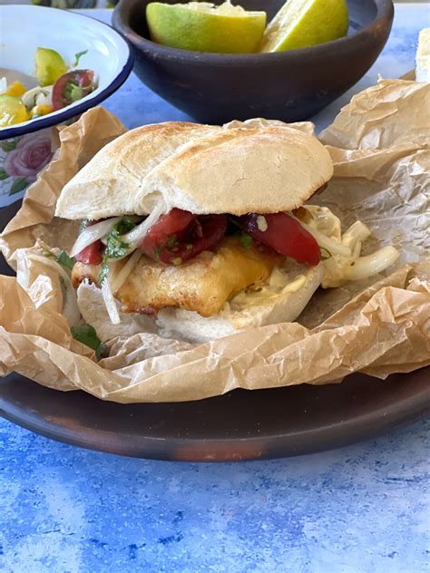 un sándwich de congrio frito servido en marraqueta con ensalada chilena