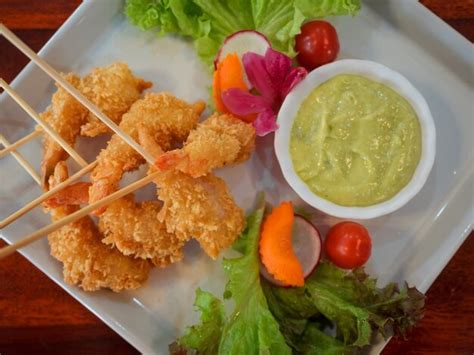 Camarones rebozados dorados y crujientes servidos en un plato, con un bol de salsa al lado.