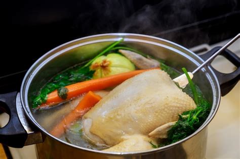 Caldo de pollo hirviendo en una olla con trozos de pollo, cebolla y zanahoria.