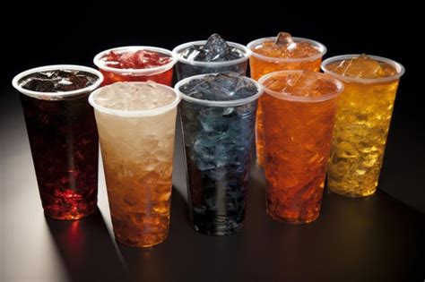 Variedad de botellas de gaseosas y vasos con jugos naturales coloridos, dispuestos sobre una mesa.