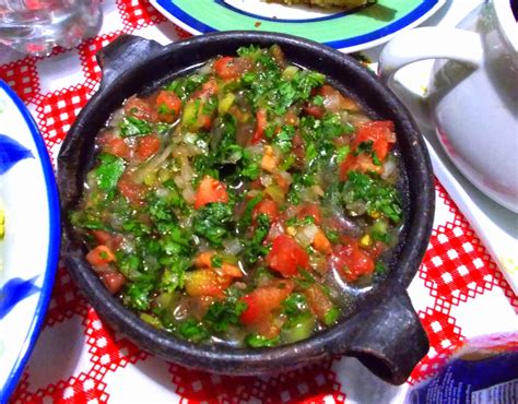 Fotografía de una mesa chilena con pebre servido en un cuenco central, pan y otros acompañamientos.