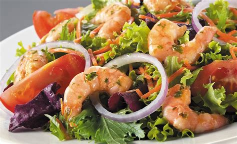 Fotografía profesional de una ensalada toscana de camarones servida en un plato, resaltando la textura de la crema y los colores de los tomates secos y espinacas.