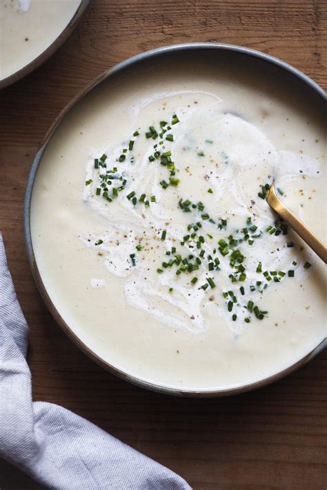 Plato de Vichyssoise servido en un cuenco elegante, adornado con cebollino fresco sobre un fondo minimalista.
