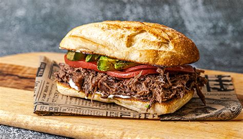Fotografía gastronómica de un sandwich de mechada servido con guarnición de papas fritas en un entorno de restaurante.