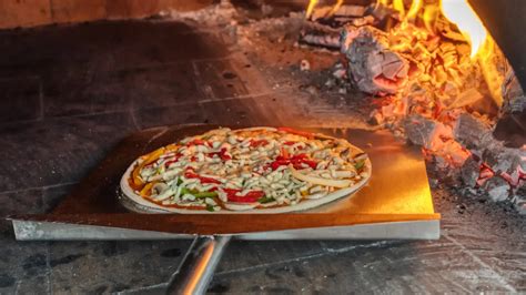 Fotografía de pizzas cocinándose en el horno de barro, utilizando una pala de pizzero.
