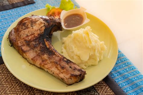 Plato servido con chuleta de cerdo a la parrilla, puré de patatas y un toque de salsa de vino.