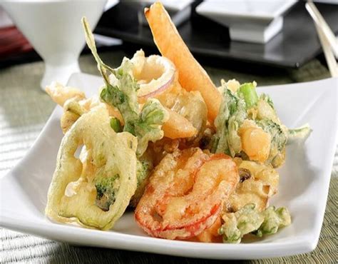 Plato de tempura de verduras variadas servido con una pequeña taza de salsa para mojar.