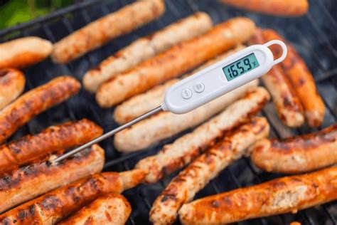 Primer plano de un termómetro para carne insertado en una salchicha asada.