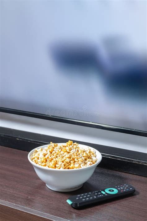 Palomitas de maíz en un bol con un mando a distancia y un televisor de fondo