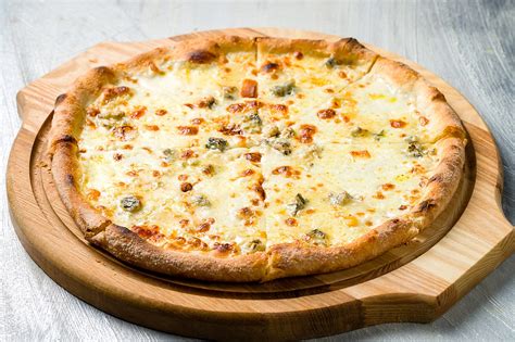 Primer plano de la pizza con los cuatro tipos de quesos distribuidos antes de hornear.