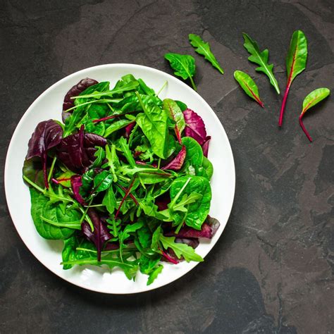 Primer plano de una ensalada de mesclun vibrante, con almendras fileteadas y semillas de girasol, aderezada con aceite de oliva y aceto balsámico.