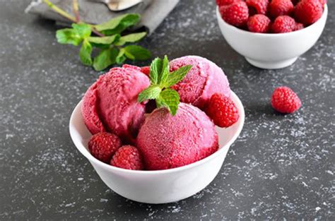 Helado cremoso de frambuesa en un bol decorado con frambuesas frescas y hojas de menta.