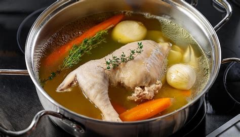 Fotografía de un caldo dorado hirviendo a fuego lento con vegetales y piezas de pollo