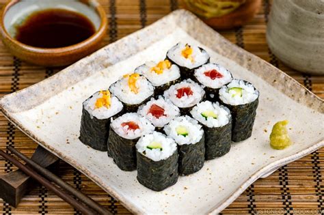 Fotografía profesional de una selección de rolls variados (Nori Maki, Hosomaki y Sashimi) presentados en una tabla de madera.