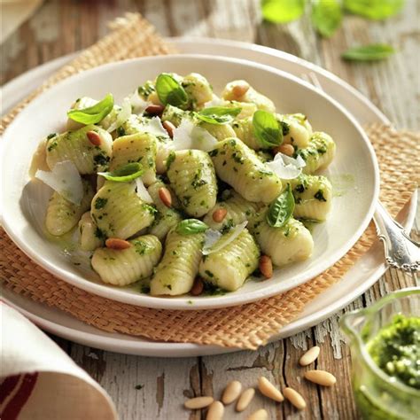 Plato servido con ñoquis de polenta y salsa pesto rosso, decorado con hojas de albahaca