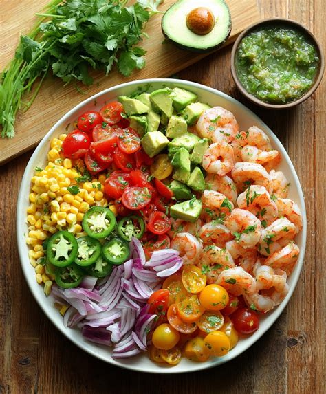 Infografía que muestra los ingredientes principales: camarones rosados, limones, cebolla morada, aguacate y cilantro sobre un fondo de madera clara