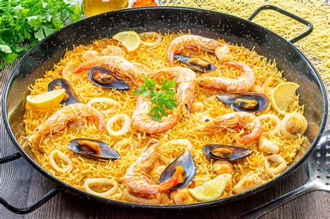 Plato de fideuá de pollo y marisco servido en una paellera tradicional con gajos de limón.