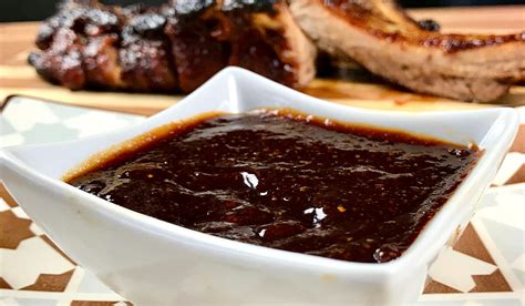Imagen de un bol con salsa barbacoa casera, decorada con miel y especias, junto a unas costillas a la parrilla.