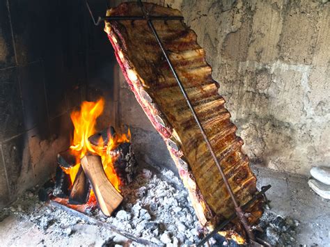 Fotografía de un costillar a la estaca cocinándose a la leña en un entorno campestre