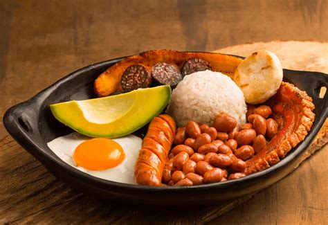 Fotografía gastronómica de una bandeja paisa con chicharrón crujiente, frijoles y arepa.