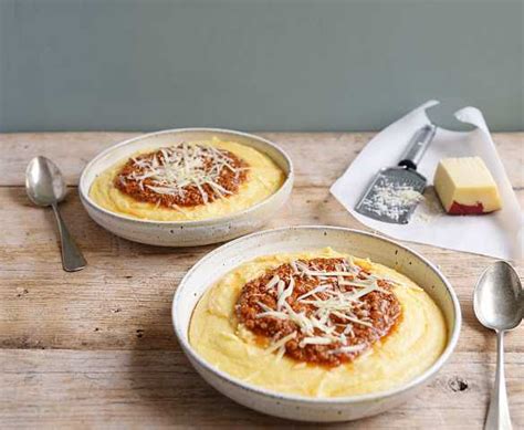 Fotografía profesional de polenta cremosa servida con salsa de carne, queso gratinado y perejil fresco.