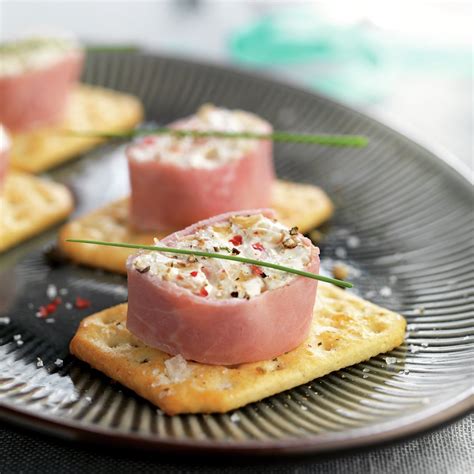 Primer plano de rollitos de jamón cocido sirviéndose sobre galletas saladas, decorados con huevas.