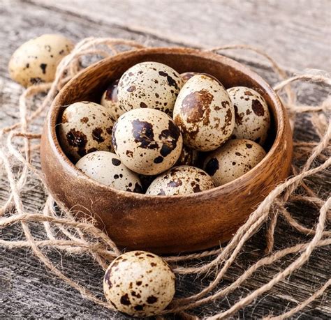 Foto de huevos de codorniz frescos y pequeños en un cuenco de madera sobre una mesa de cocina