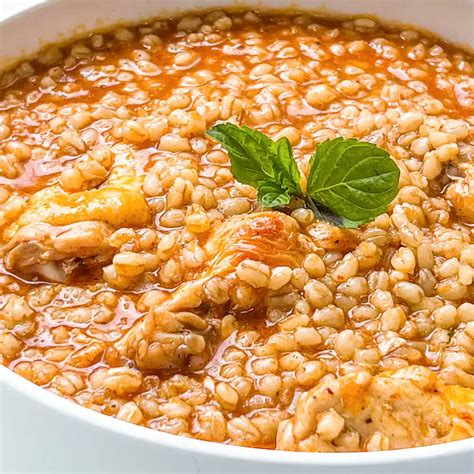 Guiso de trigo humeante en un cuenco rústico con cuchara de madera, con verduras frescas alrededor.