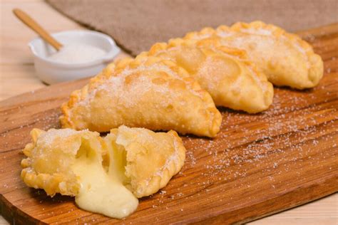 Presentación gourmet de empanadas fritas de queso en una tabla de madera con dips acompañantes