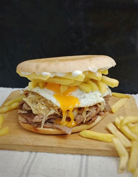 Fotografía profesional de un sándwich de churrasco a lo pobre con carne jugosa, huevo frito, papas fritas y palta, servido en un pan artesanal