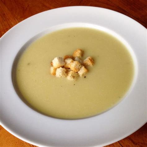 Plato servido de crema de ajo porro y papa, adornado con crutones y cebollín picado.