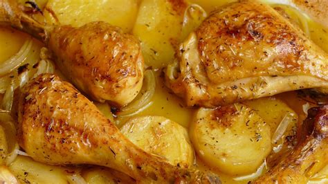 Plato de muslos de pollo dorados al horno con guarnición de patatas doradas y hierbas aromáticas