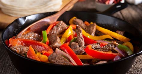 Fotografía profesional de un plato de fajitas de res servidas con vegetales coloridos y tortillas calientes.