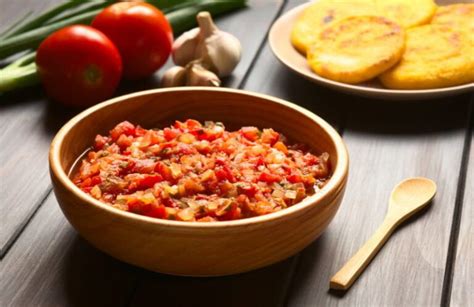Ingredientes frescos para preparar Hogao, incluyendo tomates maduros, cebolla larga y ajo.