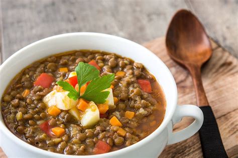 Plato de sopa de lentejas humeante con hierbas frescas