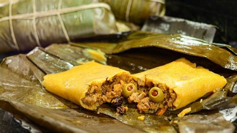 Fotografía cenital de una hallaca abierta sobre hoja de plátano mostrando el guiso y los ingredientes decorativos.
