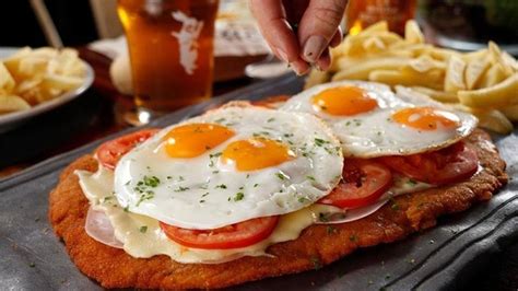 Foto de una milanesa gigante con diversas coberturas en un bodegón