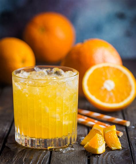 Fotografía de un vaso de naranjada casera servida con hielo y decorada con rodajas de naranja.