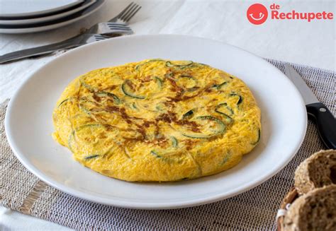 Imagen de una tortilla de calabacín jugosa servida en un plato junto a unas rebanadas de pan