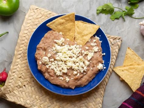 Imagen de un plato de frijoles refritos veganos servidos con totopos y pico de gallo.