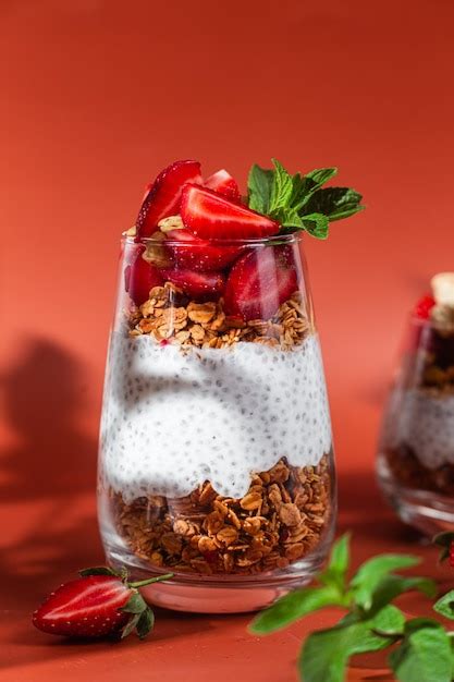 Un vaso de pudín de chía, con capas visibles de semillas y cubierto con frutas frescas y granola.