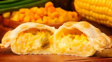 Fotografía gastronómica de empanadas de humita doradas al horno con un corte que muestra el relleno cremoso de choclo y queso.