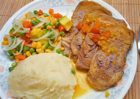 Plato servido con lengua en salsa, puré de papa y ensalada.