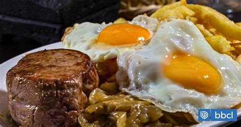 Composición visual del bistec a lo pobre, mostrando bistec, papas fritas, huevo frito y cebolla caramelizada.
