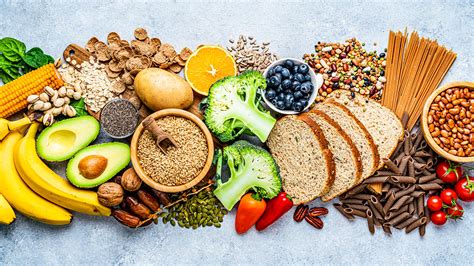 Infografía comparativa mostrando el contenido de carbohidratos, fibra y proteínas en 100 gramos de fideos, arroz, pan y cereales integrales.