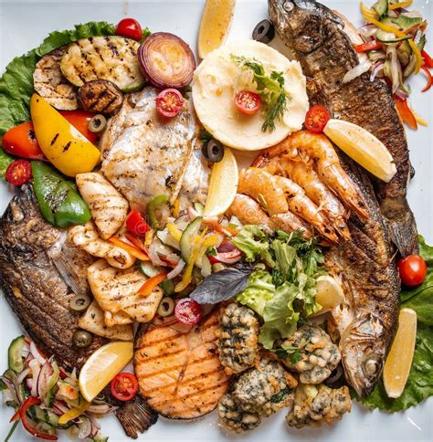Gran fuente de marisco variado (langostinos, gambas, nécoras) bien organizado por tipos, sobre una mesa con un mantel de tonos cálidos y copas de vino blanco.