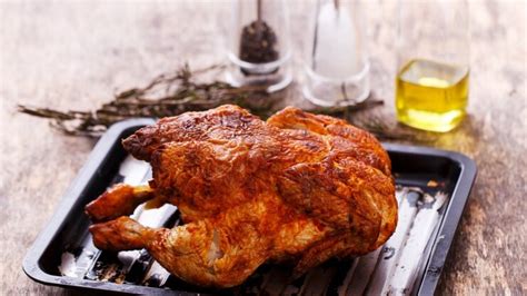 Plato de pollo rostizado entero con guarniciones y hierbas