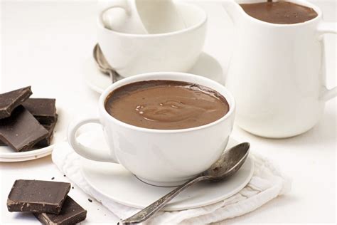 foto de una taza de chocolate caliente con espuma servida junto a un batidor de mano